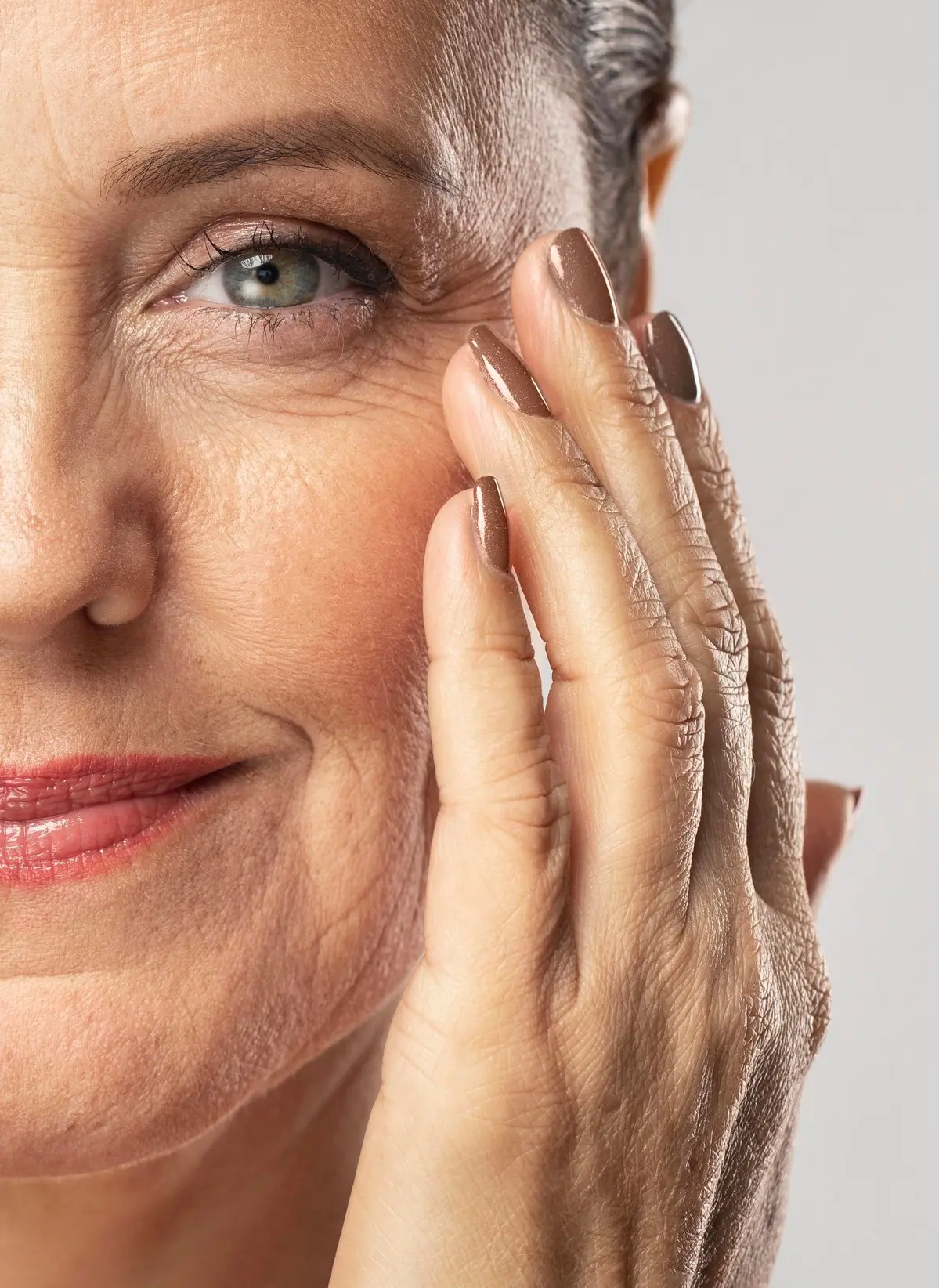 Mitad izquierda del rostro de una mujer de edad madura que necesita una blefaroplastia en Málaga, tocándose con delicadeza las patas de gallo